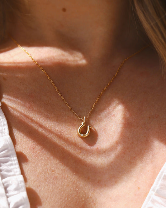 Gold and diamond horseshoe charm on cable chain being worn on a woman's neck